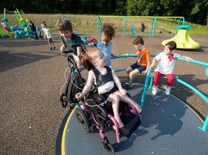 Young girl in a wheelchair playing on an inclusive spinner with other children.